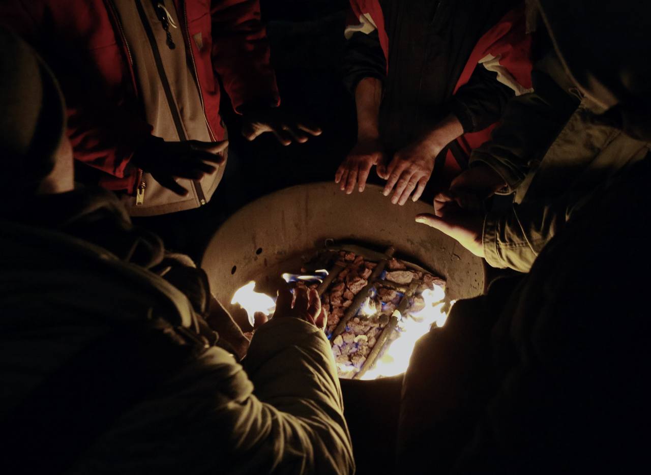 Several people hold their hands over a fire in a metal container.